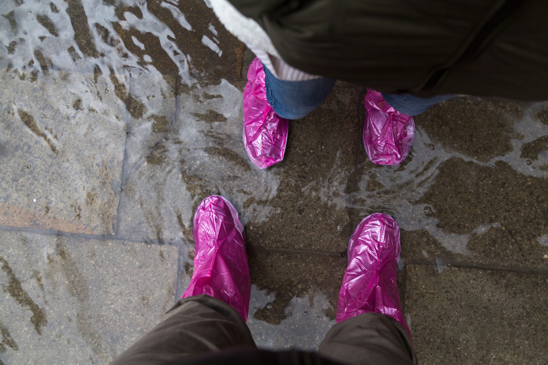 Deux paires de pieds posés sur le pavé de la place, en bottes plastique fluo pataugent dans l'eau qui déborde de la lagune.