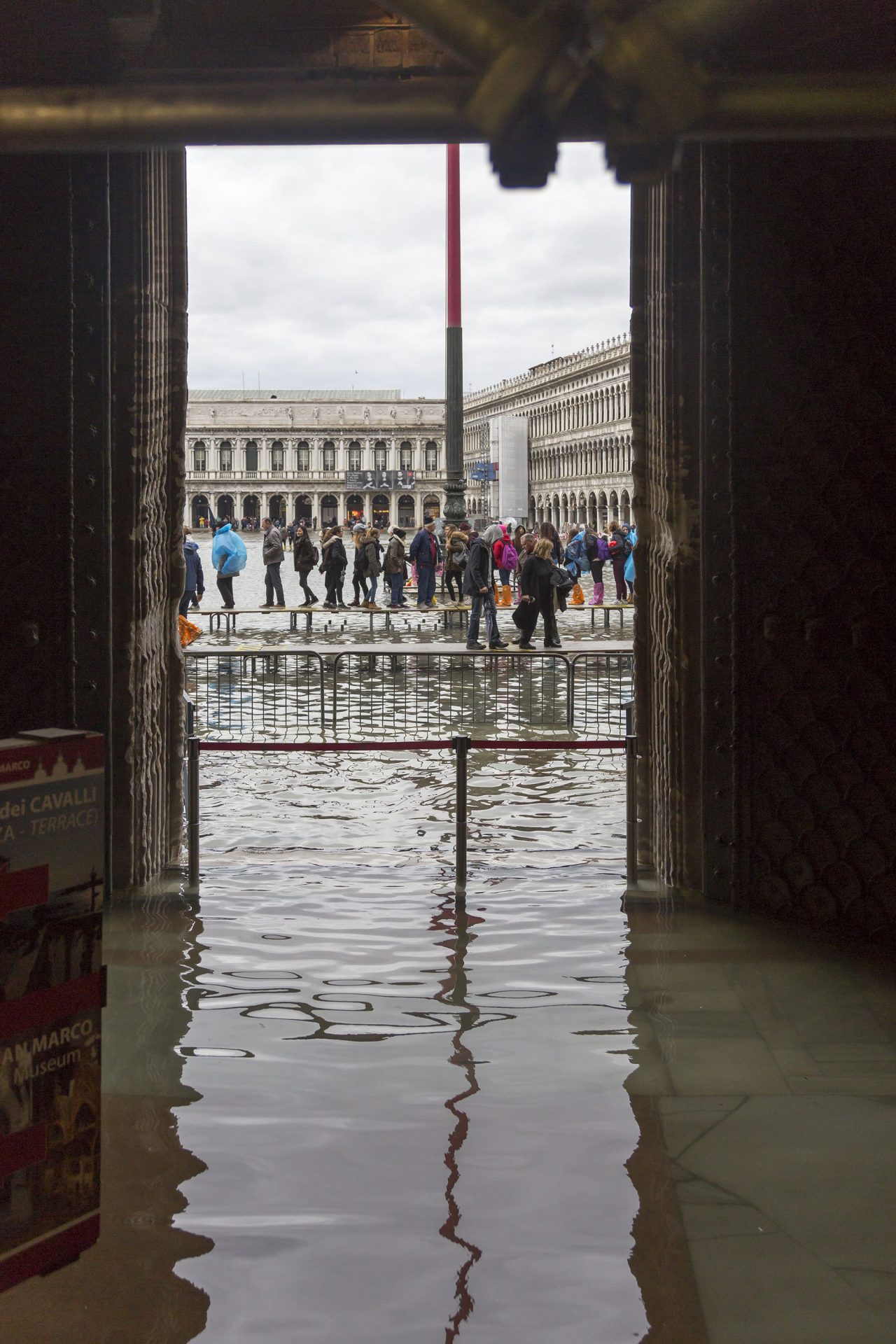Depuis le palais inondé, le portail ouvert laisse apercevoir comment les visiteurs organisent leurs chemins en file indienne perchée sur des bancs alignés.