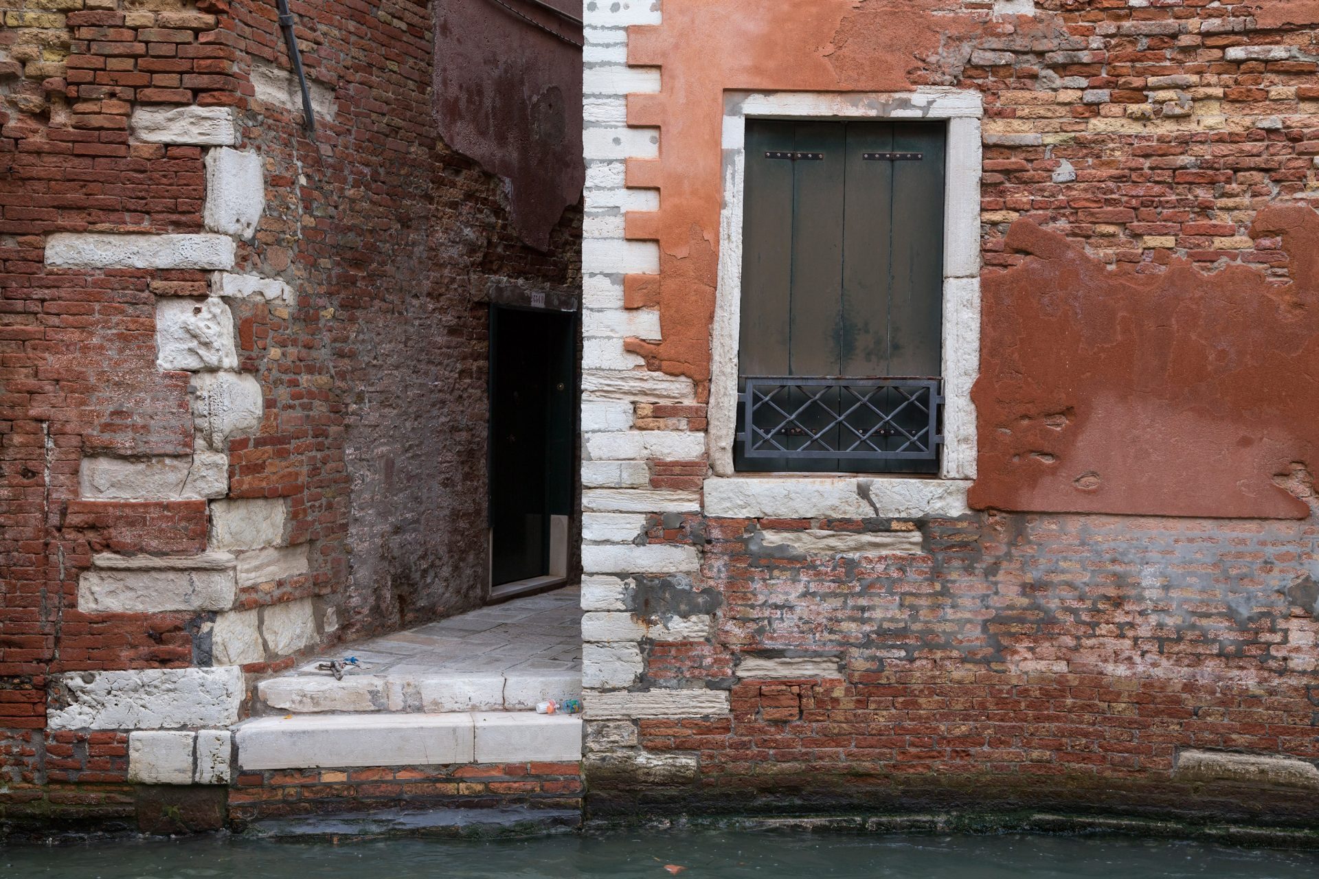 Une ruelle étroite cernée comme un couloir entre deux murs rouges se jette d'une marche dans le canal