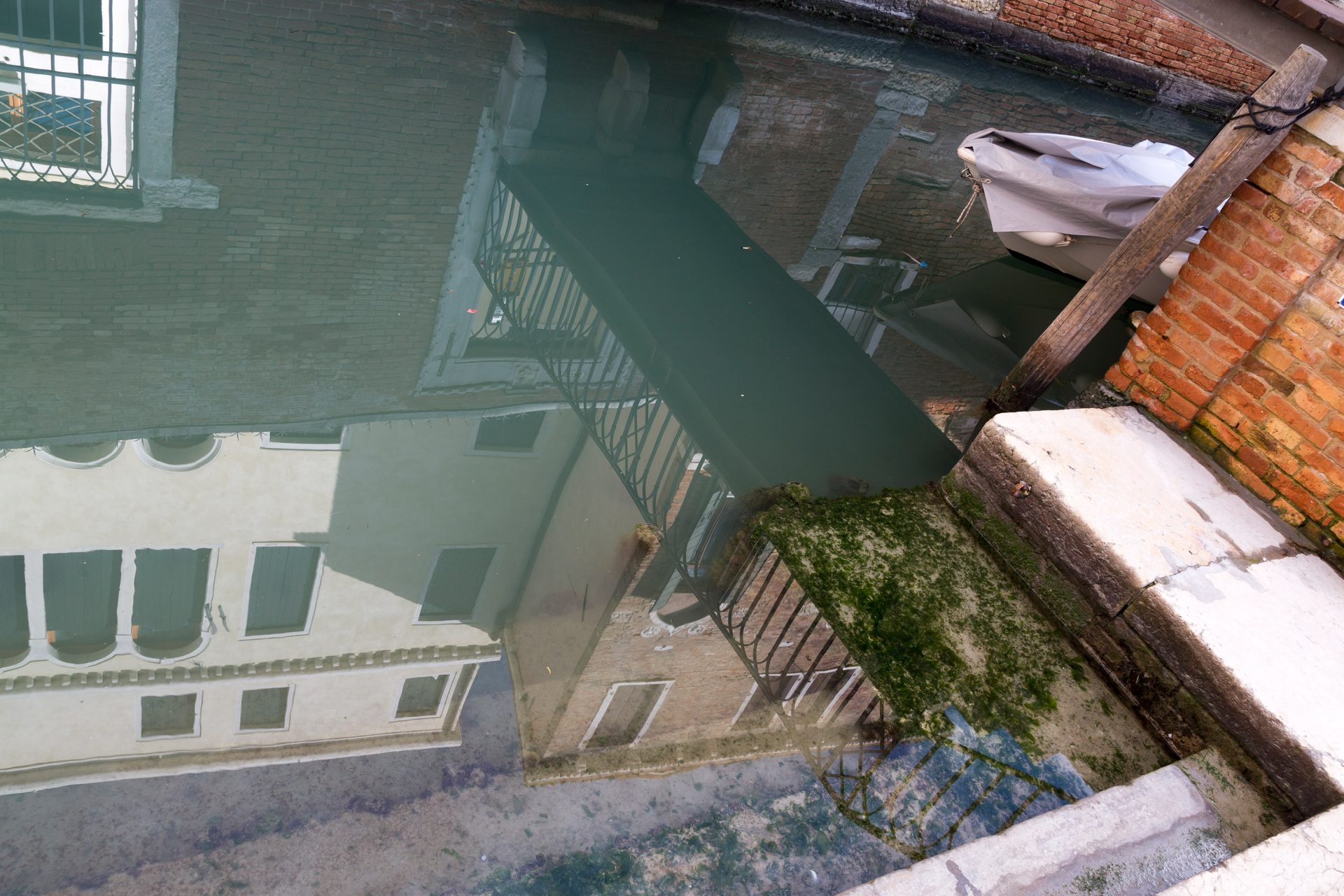Un quai d'angle par les marches duquel on descend dans le canal. La surface de l'eau est tellement lisse et transparente, le reflet des façades des villas est tellement vif que l'image du fond se mêles aux reflets aériens.