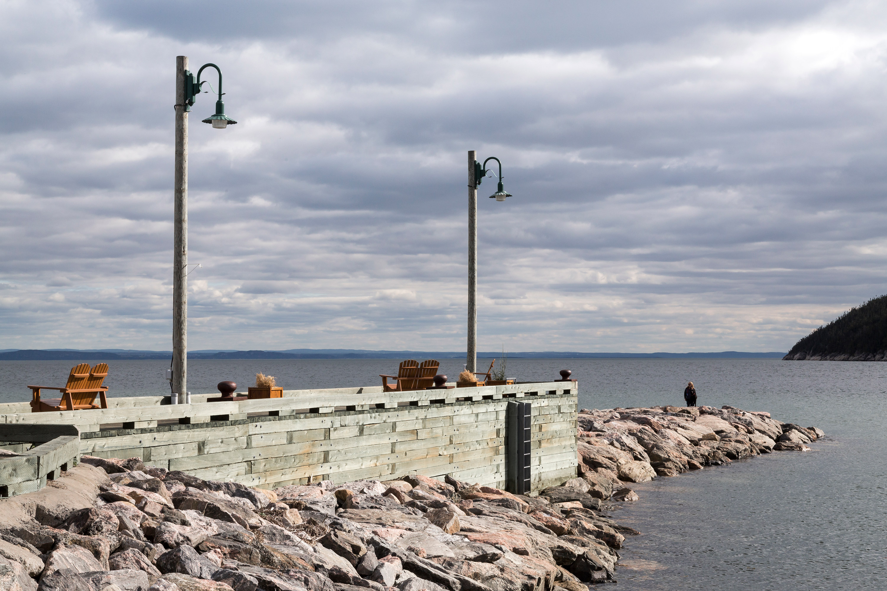 Une jetée en bois carapacée de granit rose abrite un port niché dans la baie. Le ciel bigaré est ombrageux.