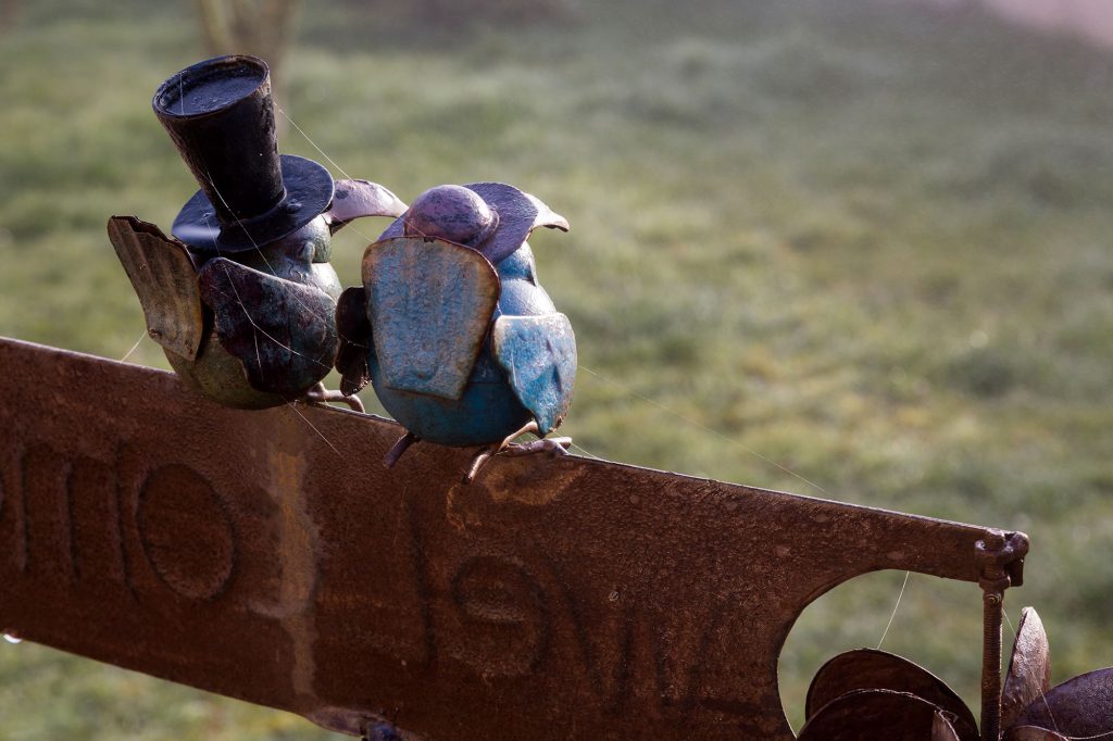 Sculpture de deux oiseaux perchés sur une pancarte "Welcome" munie d'un anémomètre